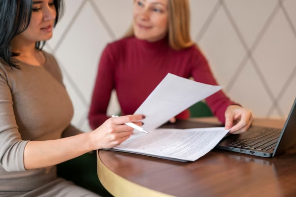 Photo de deux femmes devant un ordinateur, qui regardent des documents. - Agrandir l'image, fenêtre modale
