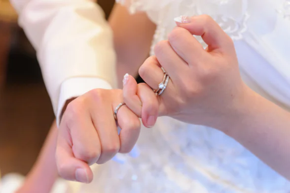 Photo des mains d'un couple de jeunes mariés dont les doigts sont entrelacés. - Agrandir l'image, fenêtre modale