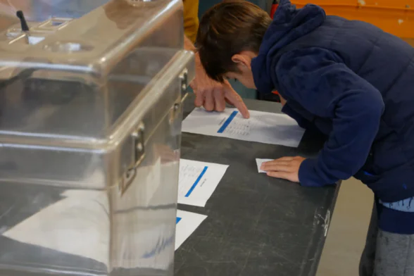 Photo d'une enfant en train de signer une feuille, après avoir voté au Conseil municipal des enfants du Haillan. - Agrandir l'image, fenêtre modale