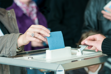 Photo d'une femme qui met une enveloppe dans une urne pour voter.