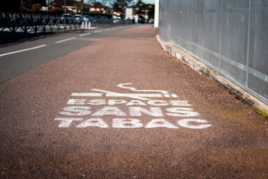 Marquage à la peinture blanche d'une cigarette barrée et inscription "espace sans tabac" sur un trottoir